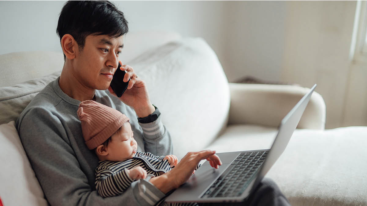 Man sitting on a sofa with a baby on his lap. He’s searching the internet and using his mobile phone